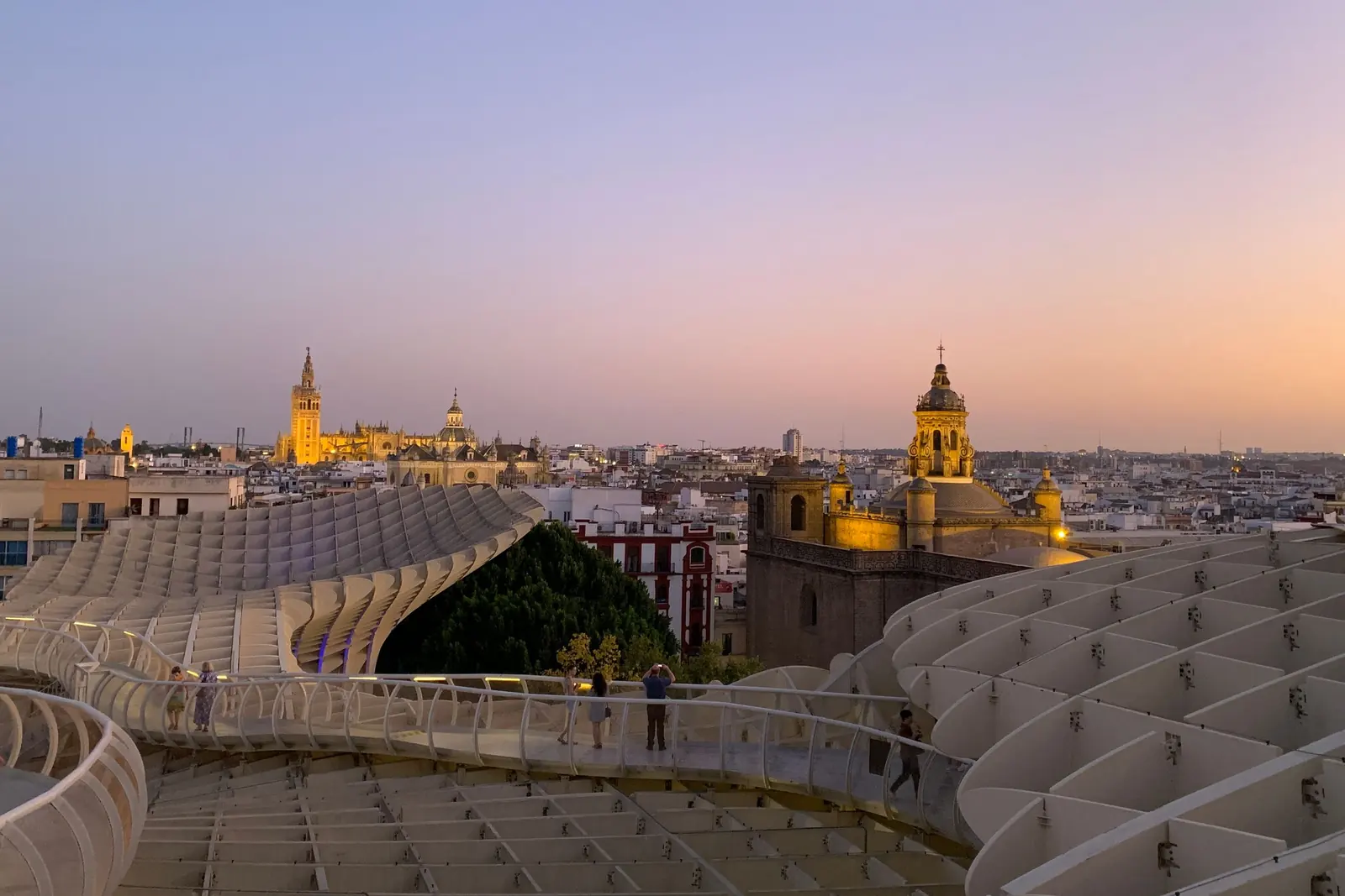 Zakřivené bílé lávky Setas de Sevilla za soumraku, s Giraldou a katedrálou osvětlenými zlatě na horizontu